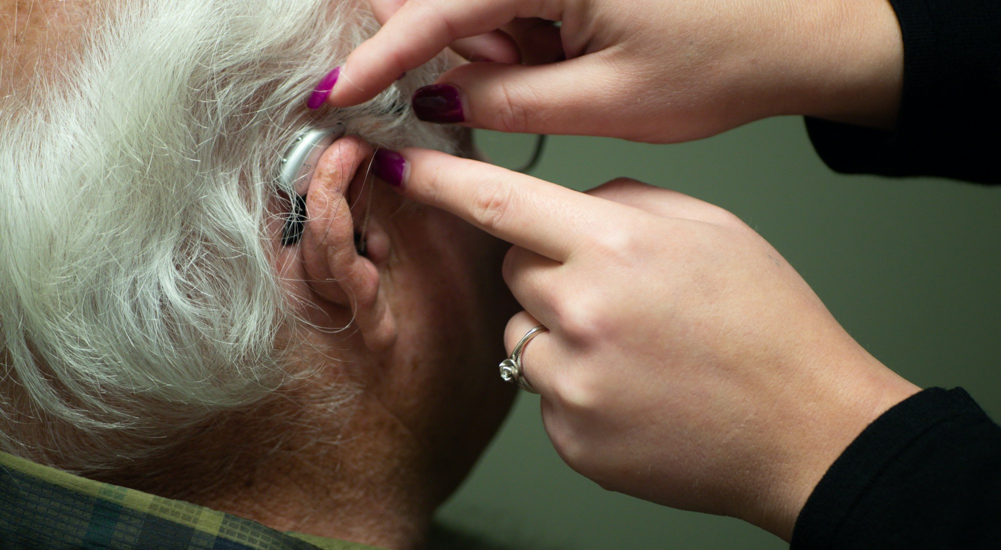 An audiologist fitting a behind-the-ear hearing aid for an elderly patient