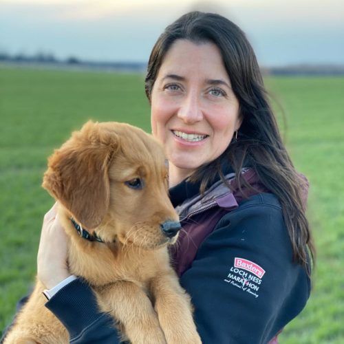 Dr. Gillian Egli of Oak West Animal Clinic holding a golden retriever puppy in a field