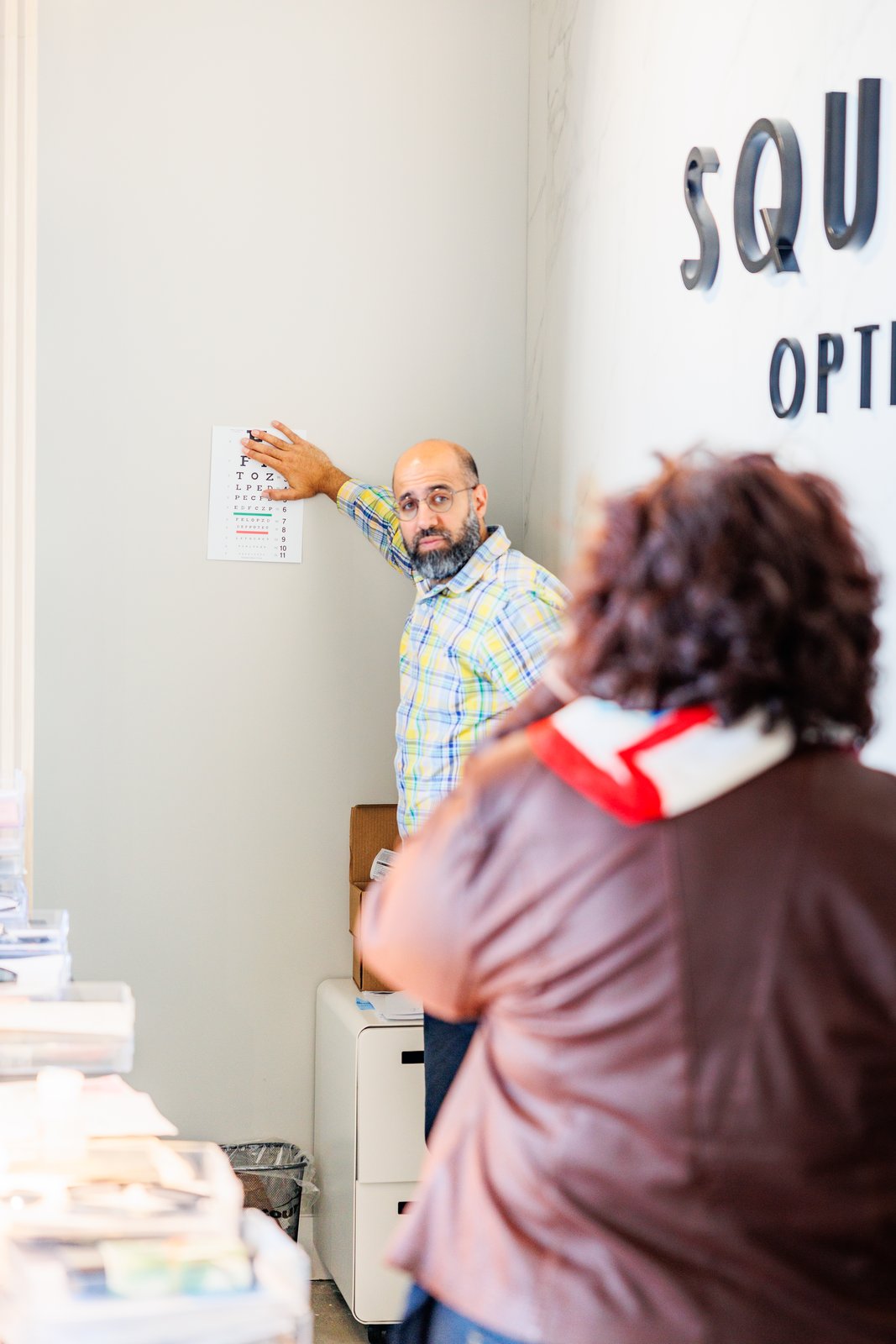 The Squints Optical optician at the eye chart with a customer, London Ontario