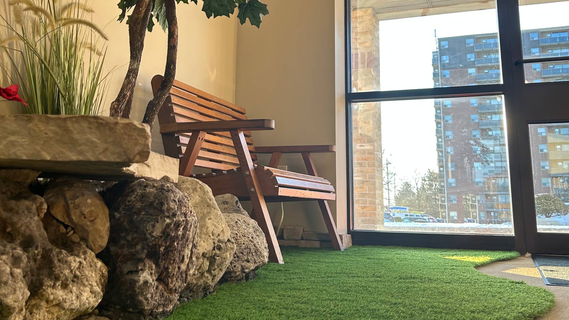 The park-themed lobby at Westmount Neighbourhood Pet Clinic, with a wooden bench on grass turf beside real boulders and a tree